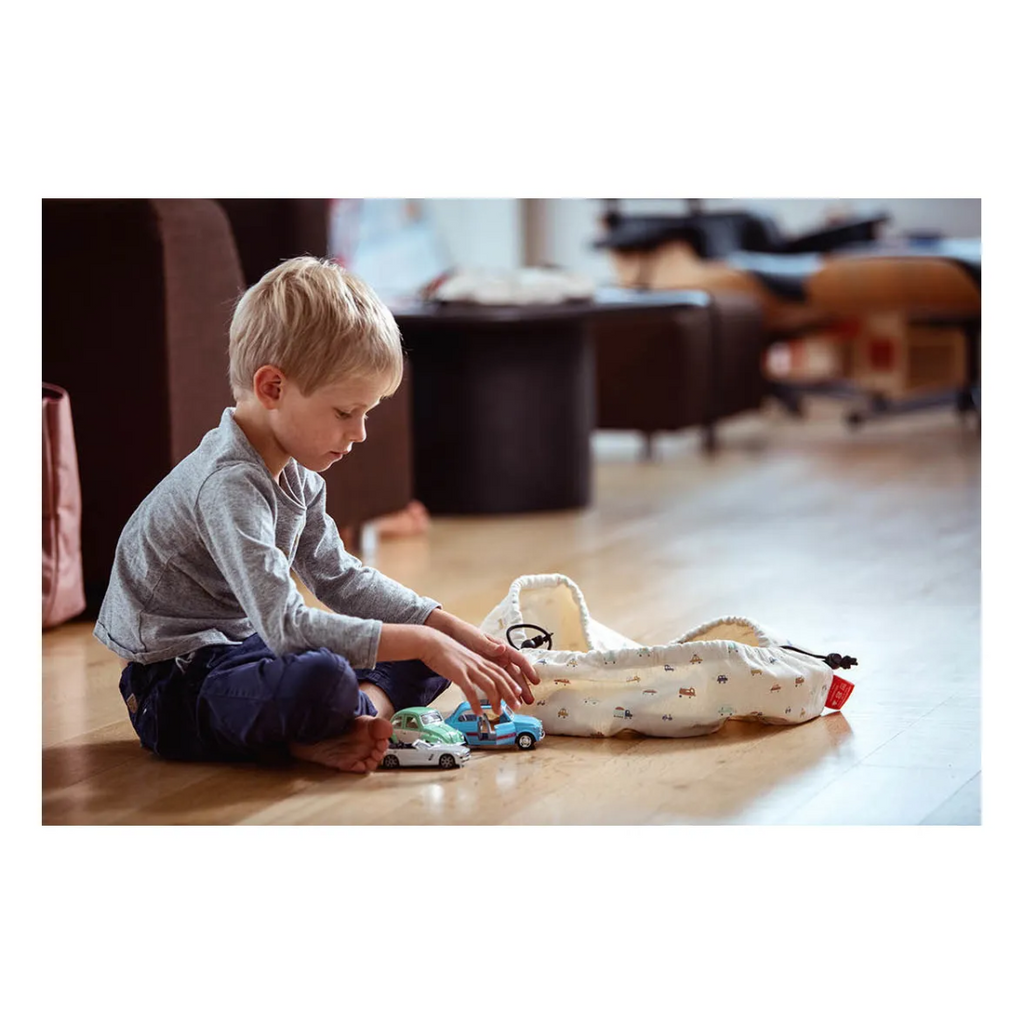 Child playing with toy cars on a wooden floor in a living room.