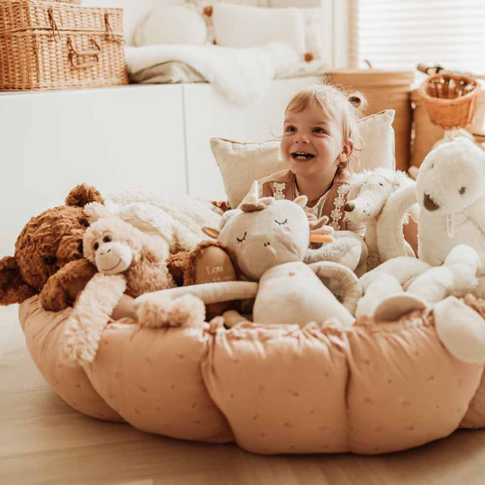 Child surrounded by stuffed animals on a play cocoon mat