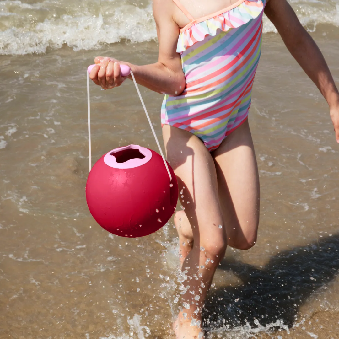 Child in a colorful swimsuit holding a red ball on a beach