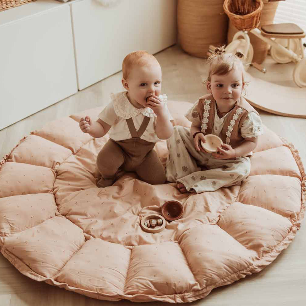 Two children sitting on a round pink cushion in a room with toys around.