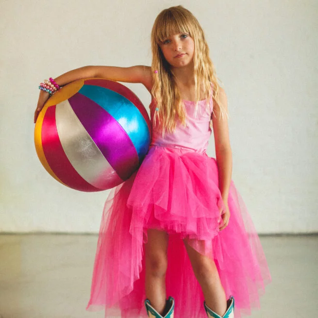 Young girl in a pink dress holding a colorful beach ball against a plain background