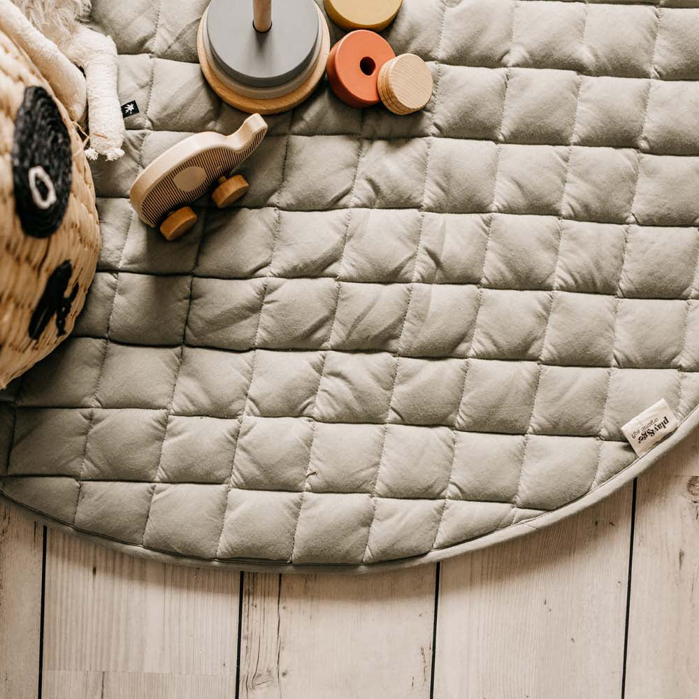 Round quilted mat on a wooden floor with toys around