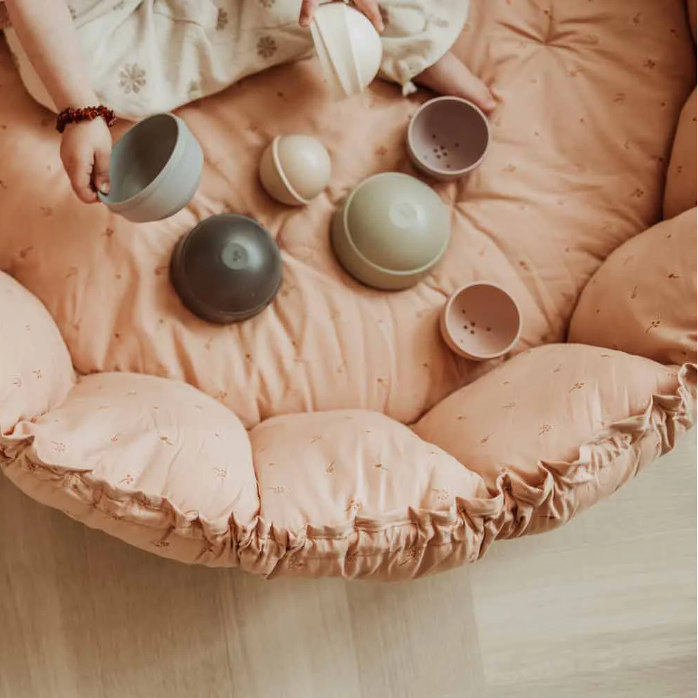Child playing with toys on a large pink cushion on a wooden floor