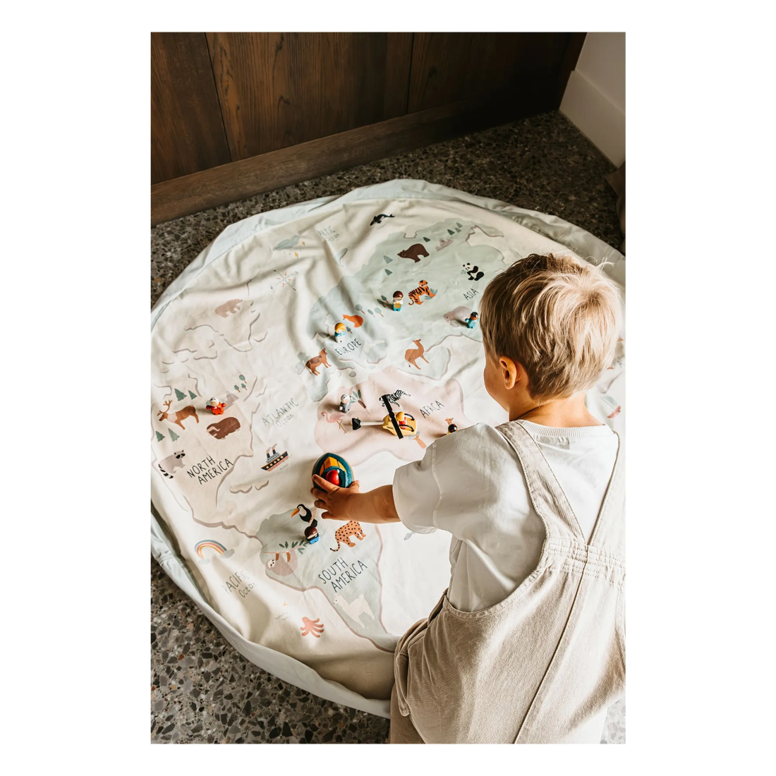 Child playing on a round mat with animal illustrations in a room.