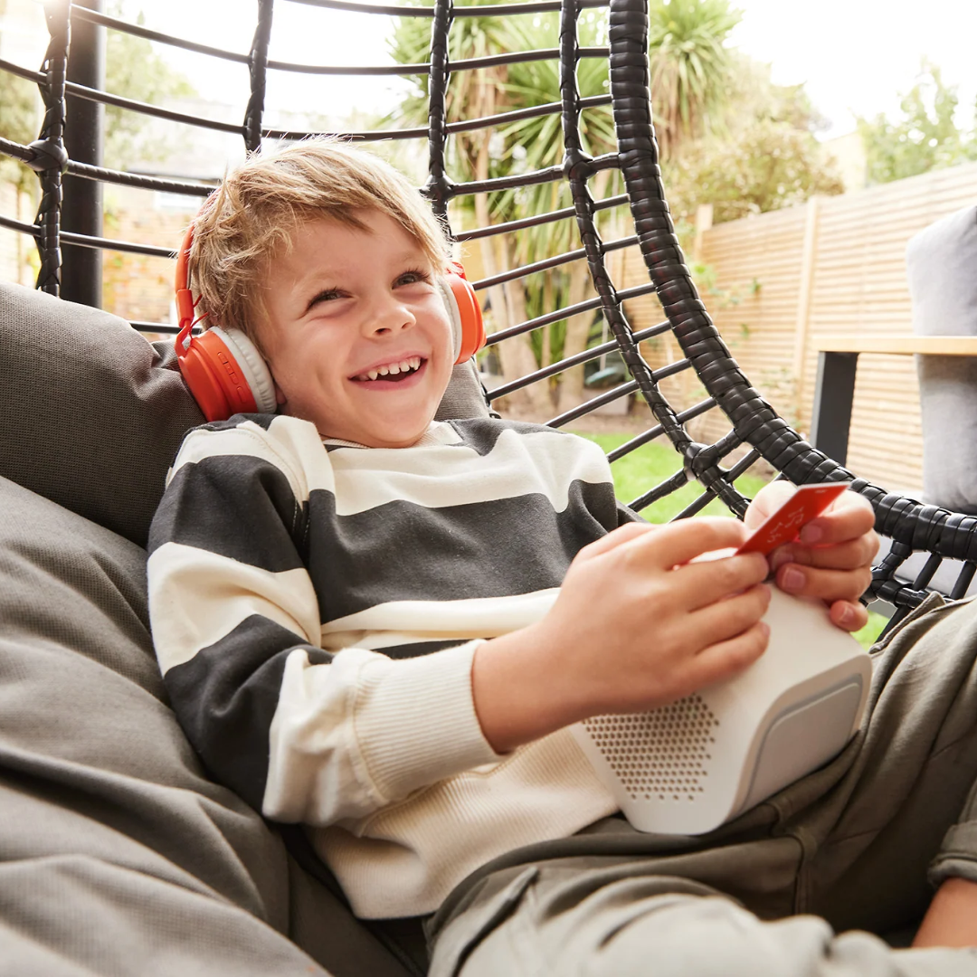 Child sitting in a swing with headphones and a Yoto player, smiling outdoors.