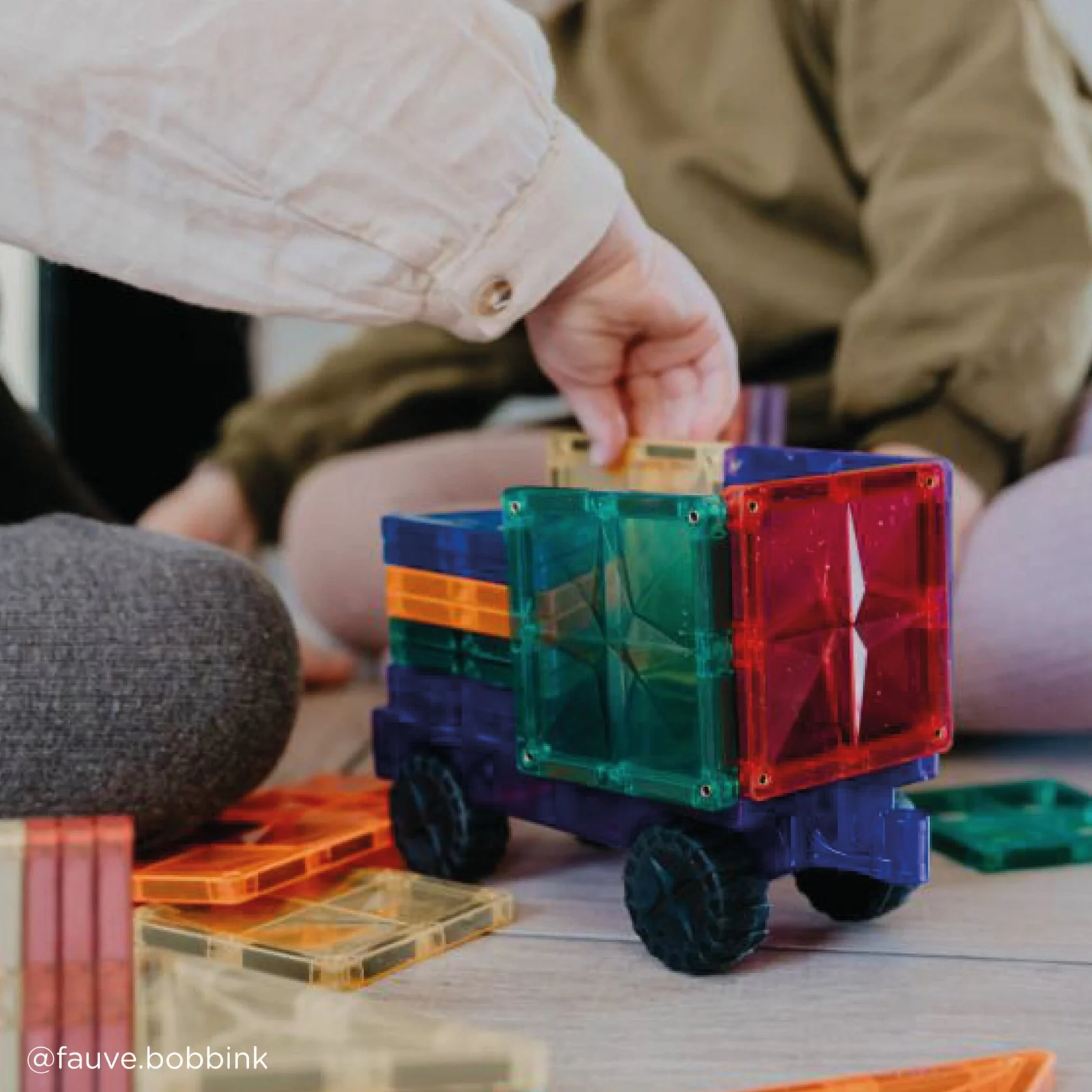 Child playing with colorful transparent magnetic blocks on a table.