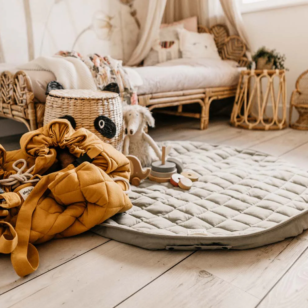 Mustard-coloured bag wrap on a wooden floor with a textured mat and wicker furniture in the background.