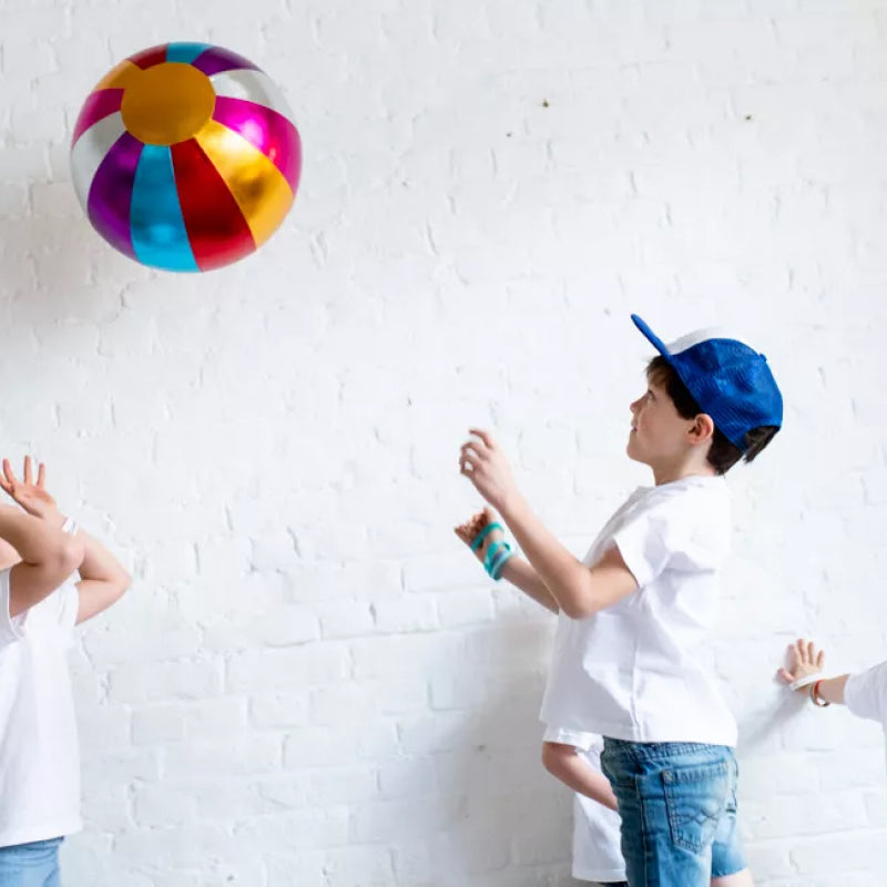 Two children playing with a colorful beach ball against a white brick wall.