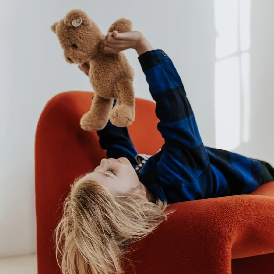 Child playing with a teddy bear on a red chair in a bright room