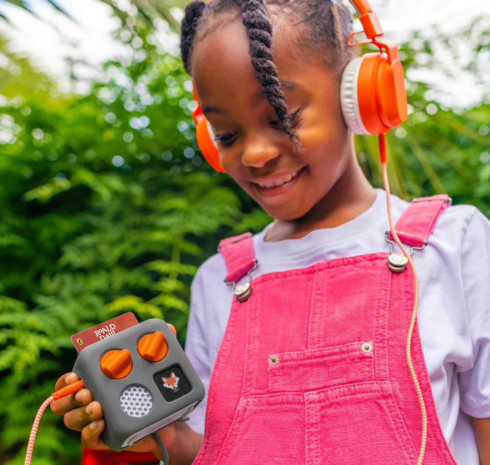 Child wearing orange headphones holding a device with a green outdoor background