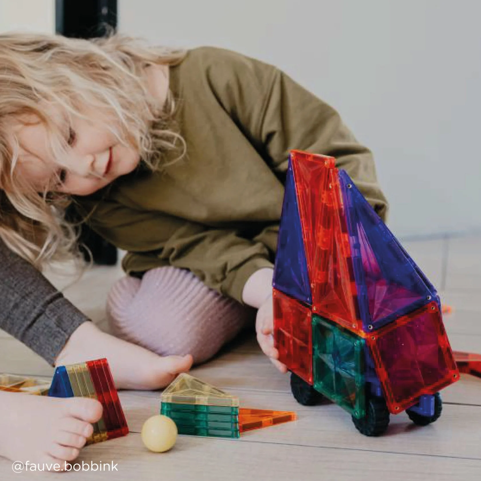 Child playing with colorful magnetic building blocks on a light surface.