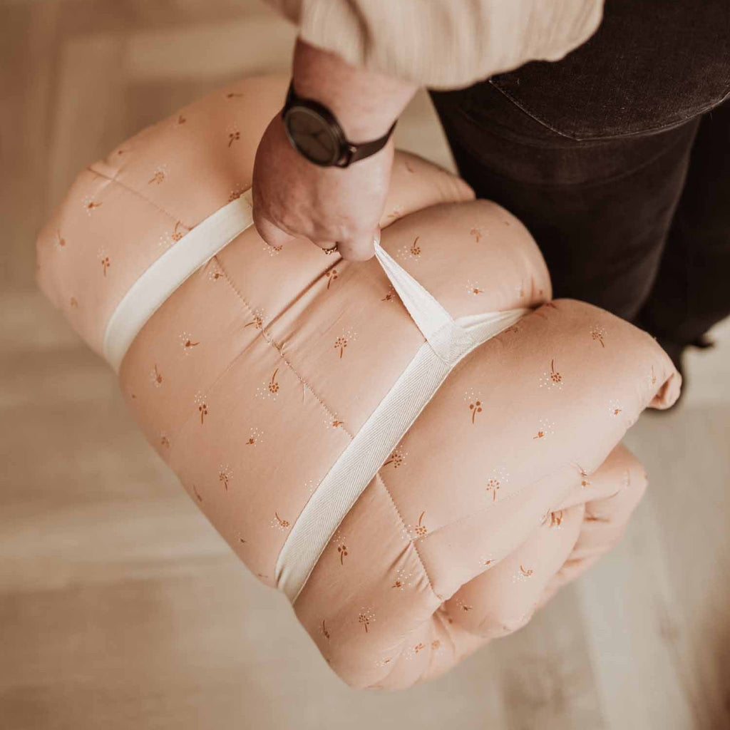 person holding play mat wrapped in its carry handle.