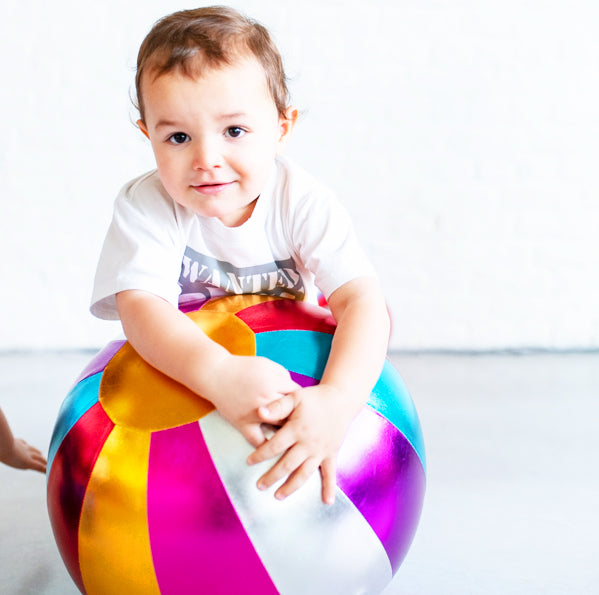 Child sitting on a colorful striped ball against a white background