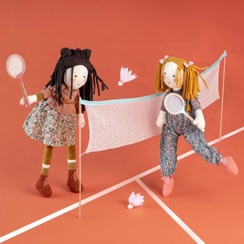 Two dolls playing badminton on a red court with a net.