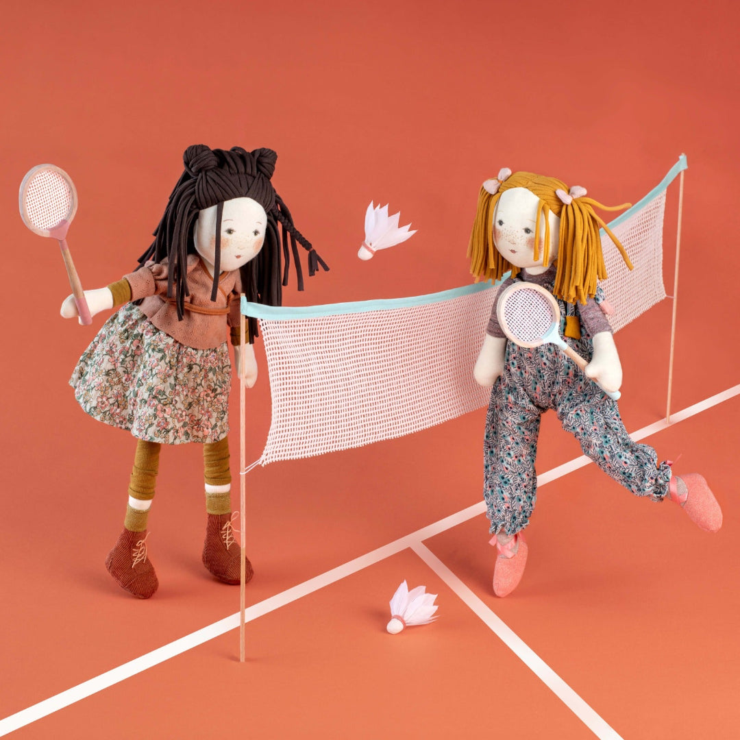 Two dolls playing badminton on a red court with a net.