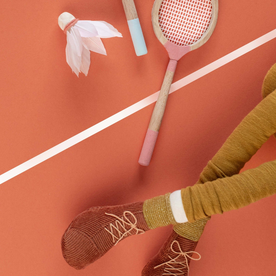 Badminton racket and shuttlecock on a red court with legs wearing socks and shoes.