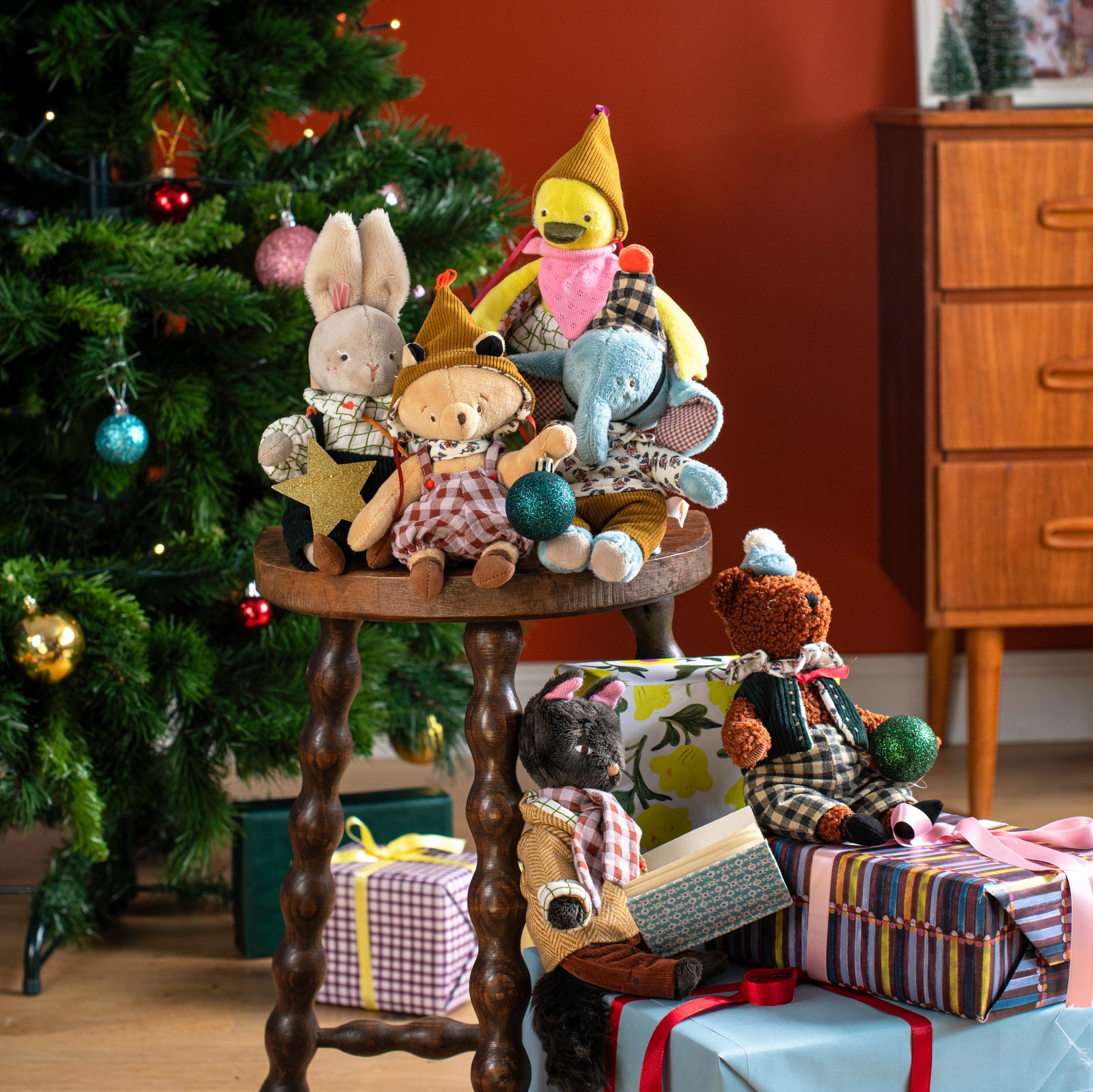 Collection of stuffed animals on a wooden stool with Christmas decorations and presents in the background.
