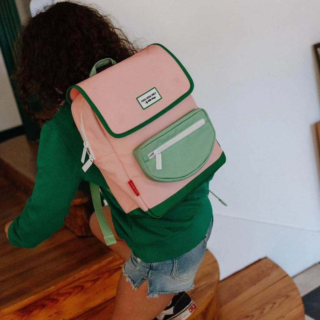 Child wearing a pink and green backpack indoors