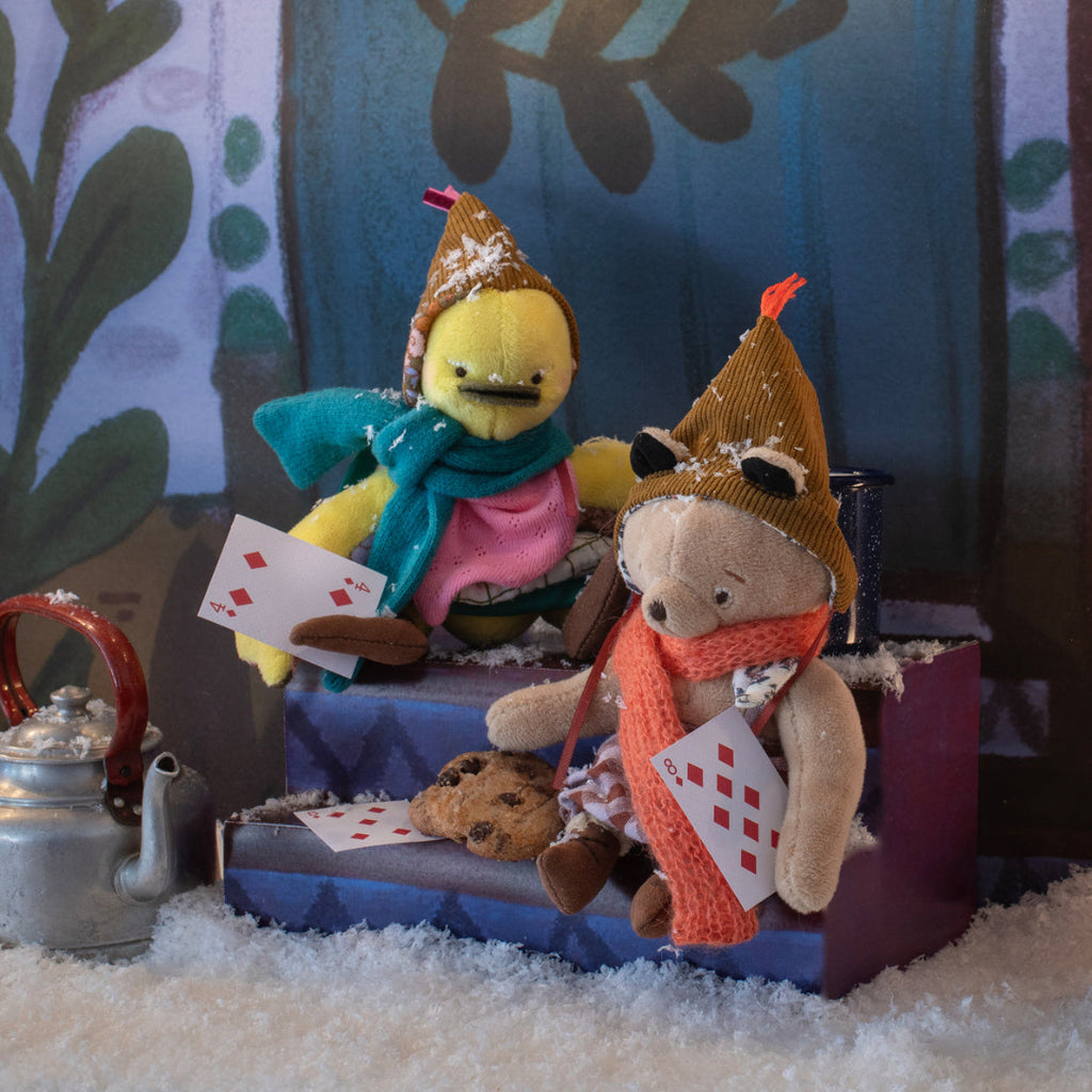 Two plush toys, one yellow and one brown, sitting on a small stage with cards and cookies.