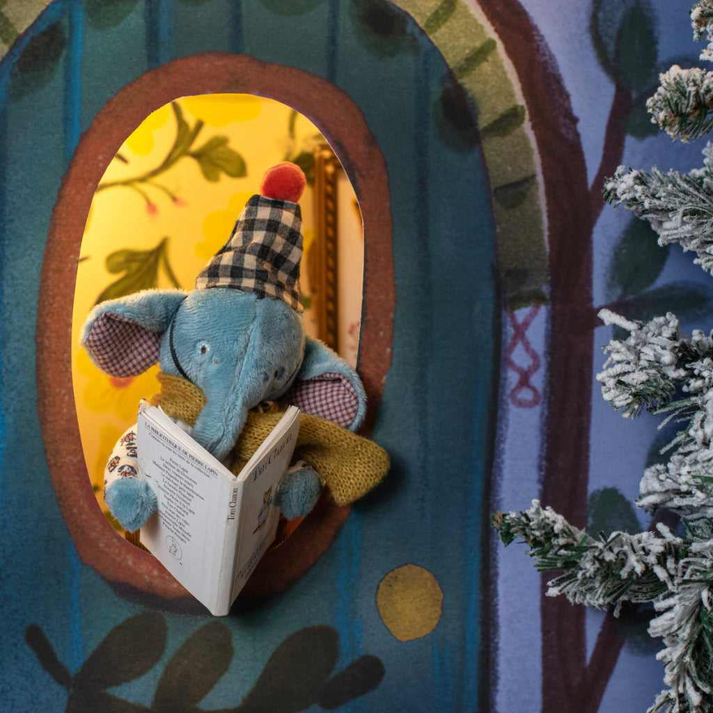 Toy elephant reading a book in a wooden frame with a snowy landscape in the background